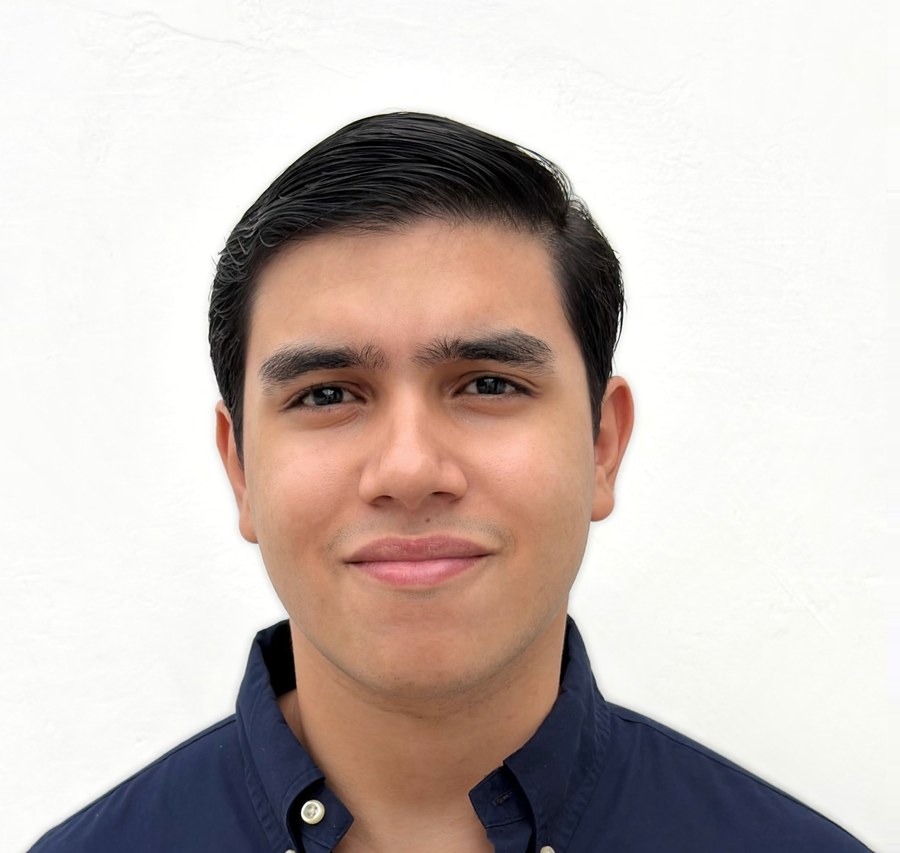 Juan Navia, from the head to the chest against a plain light wall, wearing a navy button-down shirt and looking straight at the camera.